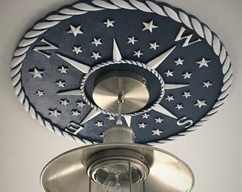May include: A white and blue compass rose ceiling medallion with a rope design border. The medallion features a compass with a silver light fixture hanging from it.