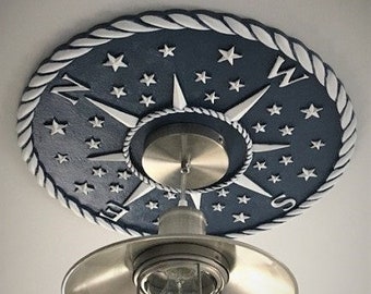 May include: A white and blue compass rose ceiling medallion with a rope design border. The medallion features a compass with a silver light fixture hanging from it.
