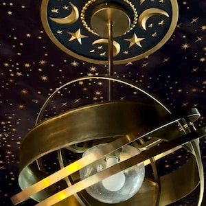 May include: A gold-toned, circular ceiling fixture with a globe-shaped light bulb. The fixture is suspended from a round, black and gold ceiling medallion with a crescent moon and star design.