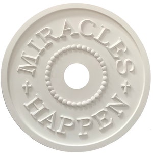以下が含まれることがあります： 中央に穴の開いた小さな円を囲むように、"MIRACLES HAPPEN"という文字が浮き彫りにされた、白い丸い天井の装飾