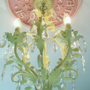 May include: A light green chandelier with crystal drops hanging from it. The chandelier is mounted to a pink ceiling with a white inscription that reads "Anything is possible."
