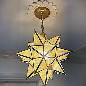 May include: A star-shaped pendant light fixture featuring textured, translucent glass panels held within a brass-toned metal frame. The light is suspended from a matching brass chain attached to a white, scalloped, circular ceiling medallion.