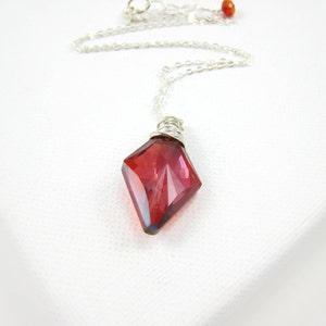 May include: A silver chain necklace with a red faceted crystal pendant. The crystal is wrapped in silver wire.