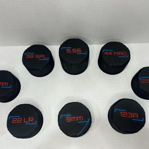 May include: Eight black, circular items, each displaying a different calibre marking in red and blue, such as "9mm" and "22 LR". The objects are arranged in a circle.