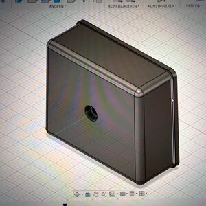 Könnte beinhalten: Ein 3D-Rendering einer rechteckigen Metallbox mit abgerundeten Ecken und einem kreisförmigen Loch. Die Box hat eine dunkle, gedämpfte Farbe, möglicherweise Grau oder Braun, und scheint ein digitales Modell oder ein Prototyp zu sein.