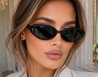 May include: Oval-shaped black sunglasses with a glossy finish and dark tinted lenses. The frames feature a smooth, rounded silhouette with small silver-toned metal accents on the outer corners near the temples, providing a clean and simple look.