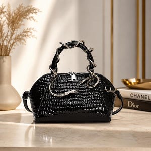 May include: A black handbag with a glossy crocodile-embossed texture, featuring a unique silver-toned metal handle shaped like a coiled snake. The bag has a structured, rounded silhouette with a top zip closure and side attachments for a strap.