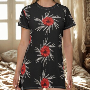 May include: Black dress with a repeating pattern of red roses surrounded by white, hand-like shapes. The dress has short sleeves and a round neckline. The fabric appears to be a soft, lightweight material.