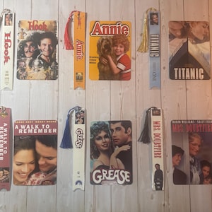 May include: A collection of rectangular movie-themed bookmarks and matching VHS-style covers featuring titles including Hook, Annie, Titanic, A Walk to Remember, Grease, and Mrs. Doubtfire. Each bookmark includes a colorful tassel attached to the top.