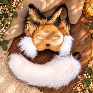 Peut inclure: Un masque inspiré d'un renard avec des oreilles en fausse fourrure brune et noire, un visage beige avec des ouvertures pour les yeux en forme d'amande et un nez noir. Une breloque étoile dorée pend à une oreille. Une longue queue en fausse fourrure blanche.
