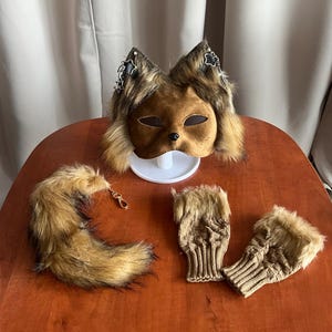 Può includere: Una maschera da volpe marrone con orecchie in pelliccia sintetica, ciondoli a stella argentati e un piccolo naso nero. Il set include una coda in pelliccia sintetica abbinata con chiusura dorata e un paio di guanti senza dita in maglia.