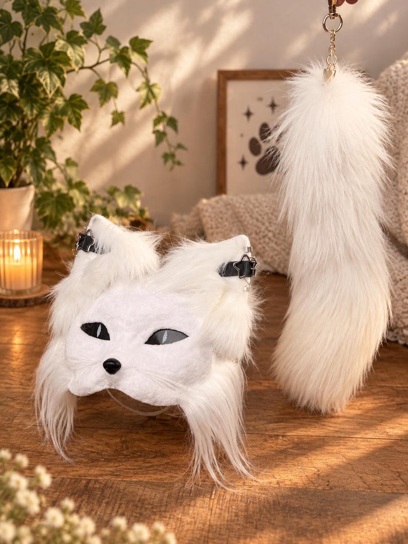 May include: A white faux fur animal mask featuring pointed ears with black star-shaped buckles, almond-shaped black eyes, and a small black nose, accompanied by a long, matching white faux fur tail attached to a gold-toned metal keychain ring.