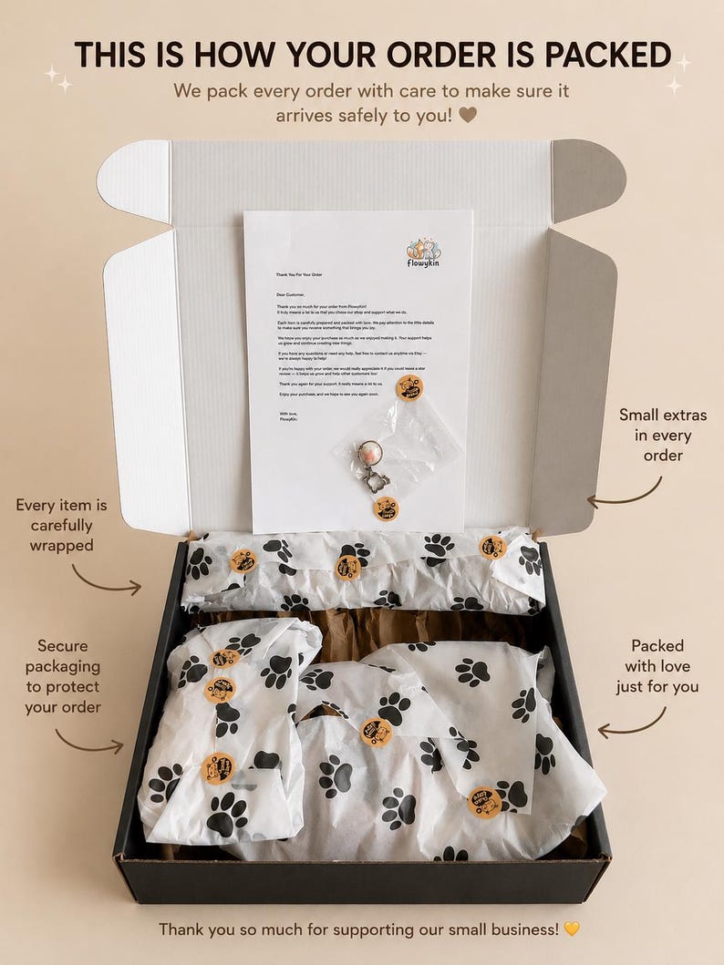 May include: An open black cardboard shipping box containing items wrapped in white tissue paper with a black paw print pattern. A thank you note from Flowykin and a small clear plastic bag with a metal charm are placed on top of the tissue paper.