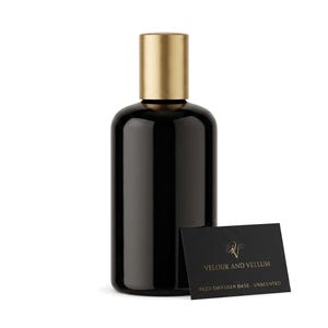 May include: A cylindrical black glass bottle with a matte gold cap. Next to the bottle is a small black rectangular card with gold text that reads Velour and Vellum, Reed Diffuser Base - Unscented, featuring a stylized gold logo at the top.