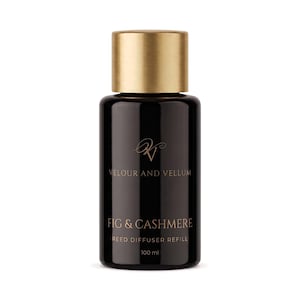 May include: A black cylindrical reed diffuser refill bottle with a brushed gold cap. The label features the text Velour and Vellum, Fig & Cashmere, Reed Diffuser Refill, and 100 ml in gold lettering. The bottle has a smooth, glossy finish.