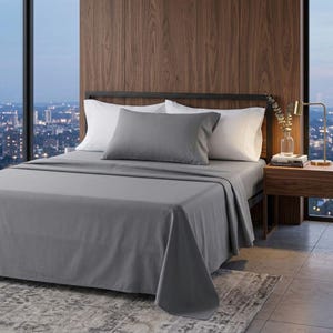 May include: A bed with gray sheets, a gray pillow, and white pillows. The bed is made up with a gray flat sheet and a gray fitted sheet. The headboard is black and the room has a wooden wall and a city view.