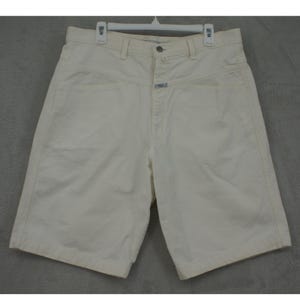 May include: Cream-coloured denim shorts with a button closure and front pockets. The shorts are hanging on a white plastic hanger. The shorts have a high waist and a straight leg design.