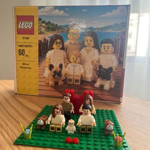 Op de afbeelding: Een LEGO Brick Memories Family and Pets bouwsetdoos met een gezin van vijf en twee honden, inclusief een bijbehorende opgebouwde scène op een groene grondplaat met vijf minifiguren, een babyfiguurtje en twee hondjes.