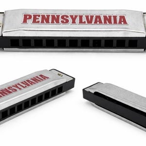 May include: A silver harmonica with black accents and the word "PENNSYLVANIA" in red letters. The image shows the harmonica from multiple angles, highlighting its design and construction.