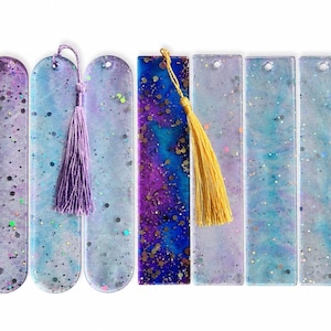 May include: A collection of six handmade resin bookmarks. The bookmarks feature a variety of colors, including purple, blue, and gold, with glitter and tassel accents. Each bookmark is rectangular with a rounded top and a hole for the tassel.