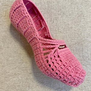 May include: A single pink crochet shoe with a pointed toe and openwork design. The shoe is handmade with a textured, woven appearance. The color is a vibrant, solid pink.