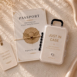 May include: A cream-colored passport holder with gold text reading PASSPORT, HINTUAN.CO, A Pause Along The Journey, and Registry No. 227-1, alongside a clear plastic case labeled JUST IN CASE with a small heart charm and a hanging tag.