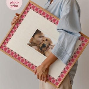 May include: A framed custom photo print featuring a photo of a person kissing a golden retriever. The frame has a light wood finish with a red and pink checkered border. The text "Custom photo print" is in a pink circle.