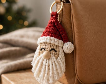 Puede incluir: Un llavero de Papá Noel tejido a ganchillo con un gorro rojo con pompón blanco, cara beige con ojos bordados en negro, nariz de cuenta de madera lisa y una larga barba blanca con flecos, unido a una anilla de metal de tono dorado.