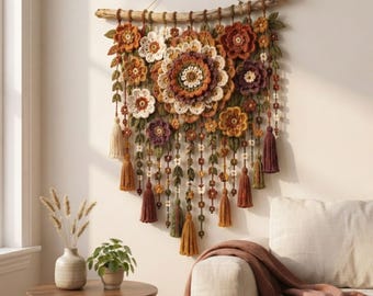 Puede incluir: Un tapiz de pared con un gran mandala central de ganchillo rodeado de varias flores y hojas de ganchillo más pequeñas en tonos naranja, marrón, crema y morado, suspendido de una rama de madera con borlas de hilo y cuentas colgantes.