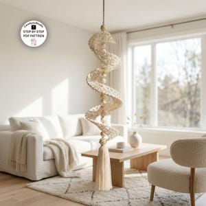 Può includere: Una decorazione a spirale sospesa realizzata in filato all'uncinetto color bianco sporco e perline di legno liscio, appesa a un cordino sottile. La struttura presenta un motivo ripetitivo di spirali all'uncinetto separate da perline e una nappa.
