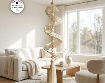 Puede incluir: Una decoración colgante en espiral hecha de hilo de ganchillo color blanco roto y cuentas de madera lisa, suspendida por un cordel fino. La estructura presenta un patrón repetitivo de espirales tejidas separadas por cuentas y una borla.
