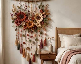 Puede incluir: Un tapiz de pared con un marco circular suspendido de una rama de madera, decorado con flores de ganchillo en tonos óxido, crema y marrón, acentuado con hojas verdes, hilos colgantes, cuentas de madera y borlas de tela coloridas.