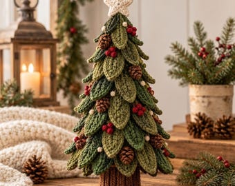Puede incluir: Un árbol de Navidad de ganchillo hecho a mano con hojas verdes en capas, pequeñas piñas marrones y detalles de bayas rojas. El árbol está rematado con una estrella de ganchillo color crema y se asienta sobre una base marrón.