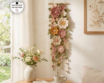 Puede incluir: Un tapiz vertical con una colección de flores y hojas de ganchillo en tonos rosa empolvado, crema y amarillo mostaza, suspendido de un listón de madera con una cuerda, con el texto Care4youStudio STEP BY STEP PDF PATTREN.