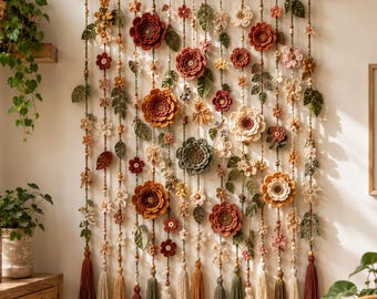 Puede incluir: Un tapiz de pared con múltiples hilos verticales suspendidos de una varilla de madera. Cada hilo está decorado con varias flores de ganchillo en tonos rojos, naranjas, crema y verdes, intercaladas con pequeñas cuentas y rematadas con borlas.