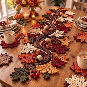 Pode incluir: Um caminho de mesa em crochê com um design de videira sinuosa adornado com várias folhas em tons de outono, pequenas bagas e bolotas. O caminho é acompanhado por bases para copos em crochê a condizer em forma de folha em tons de vermelho, laranja e creme.