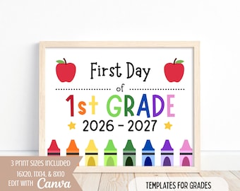 May include: A rectangular sign in a light wood frame featuring the text First Day of 1st GRADE 2026-2027. The design includes two red apples, yellow stars, and a row of eight colourful crayons in red, orange, yellow, green, dark green, blue, purple, and pink.