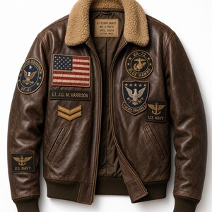 May include: A brown leather flight jacket with a tan shearling collar, featuring various military-style patches including a U.S. flag, U.S. Navy insignia, and squadron emblems. The interior label reads G-1 FLIGHT JACKET MIL-J-7823C SPEC. 55J14.