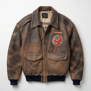 Puede incluir: Una chaqueta tipo bomber de cuero marrón desgastado con cuello oscuro, puños y dobladillo acanalados. El frente muestra dos bolsillos con solapa, un parche rectangular y uno circular con una silueta roja. Un parche está en la manga.
