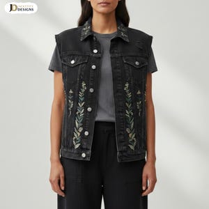 Könnte beinhalten: Eine schwarze Jeansweste mit floraler Stickerei. Die Weste hat einen Kragen, einen Knopfverschluss und dekorative Stickereien auf der Vorderseite und den Schultern. Die Stickerei umfasst grüne und cremefarbene Blumenmuster. Die Weste ist ärmellos und hat einen Used-Look.