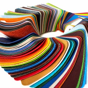 May include: A circular fan-shaped collection of fabric swatches featuring a wide spectrum of colors including red, orange, yellow, green, blue, purple, black, white, and brown. Each swatch has a textured surface and is bound together at one end.