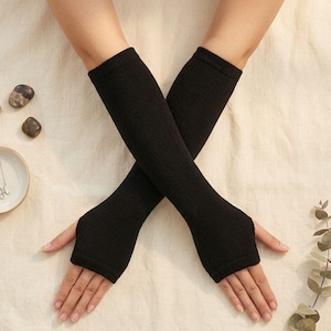 May include: Black fingerless gloves, extending to the mid-forearm, are displayed against a neutral background. The gloves are made of a textured knit fabric. The hands are positioned in an X shape, showcasing the gloves' design.
