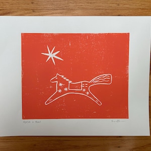 May include: A white print on a red background features a stylized horse and a star. The horse is in motion, with a decorative saddle. The text "HORSE + STAR" is at the bottom of the print.