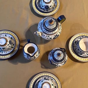 以下が含まれることがあります： 花柄の陶器製ティーセット。 ティーポット、クリーマー、シュガーボウル、カップ、ソーサーが含まれています。 青と緑のアクセントと黄色の縁が付いた白いベースが特徴です。伝統的なティーセット。