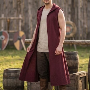 May include: A sleeveless, floor-length maroon hooded vest worn over a beige crew-neck tank top, paired with dark brown trousers and brown leather boots. The vest features an open front design, a hood, and a straight hemline reaching the ankles.