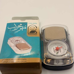 Könnte beinhalten: Ein Kompass- und Gebetszähler-Set mit einer Box. Die Box ist türkis und goldfarben mit Text in einer Fremdsprache. Der Kompass hat ein weißes Zifferblatt mit roter Nadel und dem Text "MEHRAB". Das Set befindet sich in einem transparenten Kunststoffgehäuse.