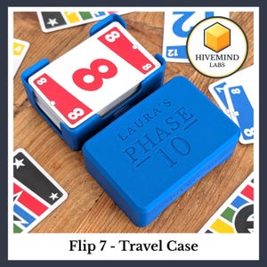 May include: A blue plastic card holder and a matching blue storage box with the embossed text LAURA'S PHASE 10. The holder contains a deck of cards featuring a red card with the number 8, surrounded by various other colourful game cards.