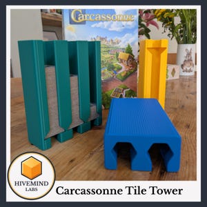May include: A teal tile holder, a yellow tile tower, and a blue tile holder are displayed in front of a Carcassonne game box. The teal holder has multiple slots for tiles. The blue holder has a ribbed surface. The text "Carcassonne Tile Tower" is at the bottom.