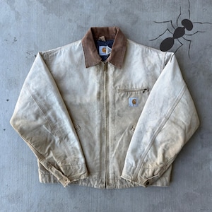 May include: A tan Carhartt jacket with a brown corduroy collar. The jacket has a zipper closure, a small chest pocket, and the Carhartt logo patch. The jacket appears worn and has a vintage aesthetic.