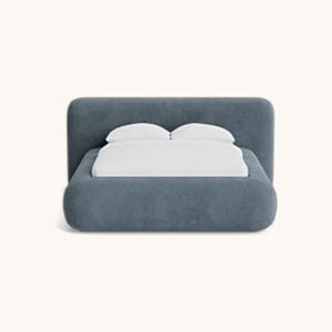 May include: A modern, upholstered bed in a muted blue-gray hue. The bed features a rounded headboard and frame, with crisp white bedding and pillows. The design is minimalist and contemporary, suitable for a bedroom setting.